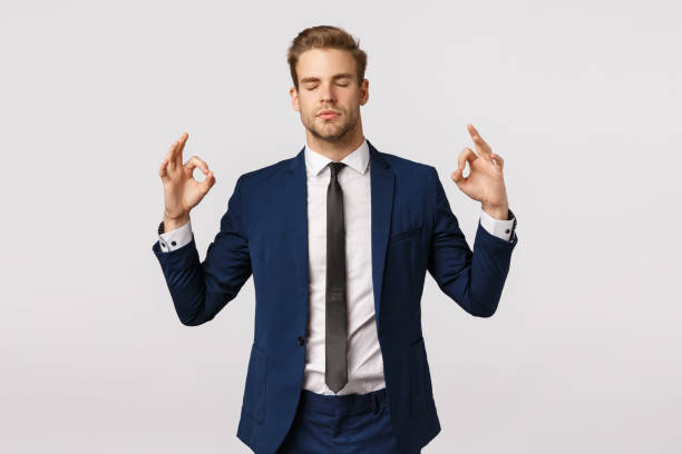 istock Dont panic, taking emotions under control. Peaceful and patient good-looking blond businessman in classic suit, make zen sign, spread hands sideways, close eyes, meditating, reliese stress 1207259645