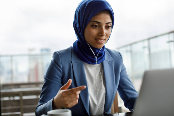 jeune femme avec des écouteurs travaillant sur l’ordinateur portatif - looking at camera photos et images de collection