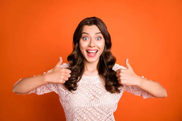 Portrait of amazed excited girl advertise show thumb-up sign suggest, select promo wear knitted blouse isolated over orange color background