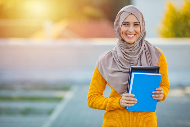 Muslim girl, a college student, holding her workbooks at student campus Muslim girl, a college student, holding her workbooks at student campus. Muslim woman with notebooks. Young Student wearing a veil and holding a copybook pics of a cute muslim outfits stock pictures, royalty-free photos & images
