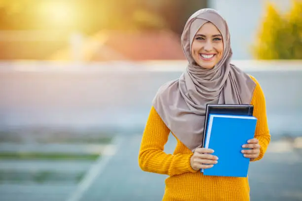Muslim girl, a college student, holding her workbooks at student campus. Muslim woman with notebooks. Young Student wearing a veil and holding a copybook