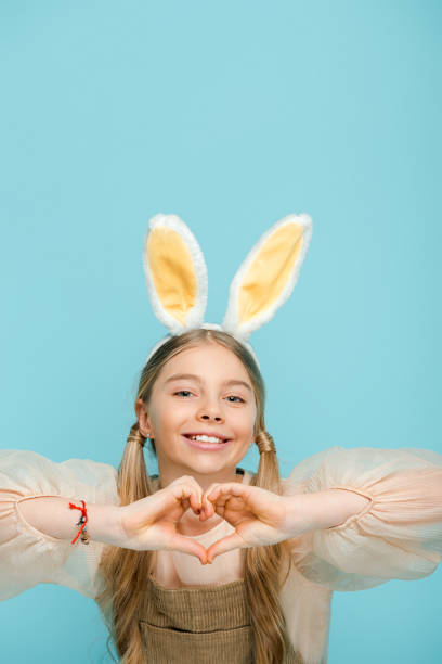 istock positive kid with bunny ears showing heart with hands isolated on blue 1207267902