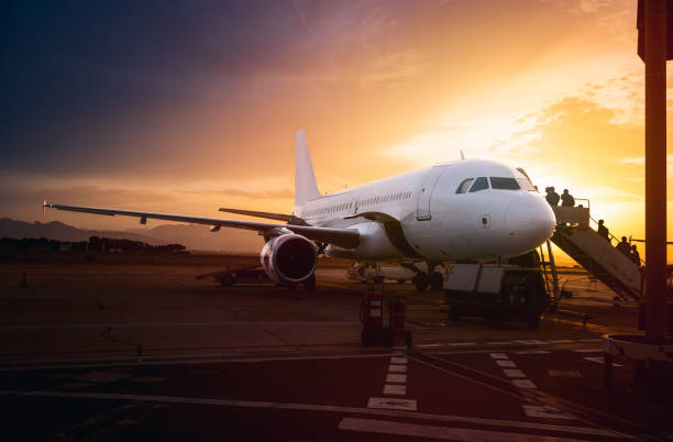 People embarking airplane at the airport with bright sunset