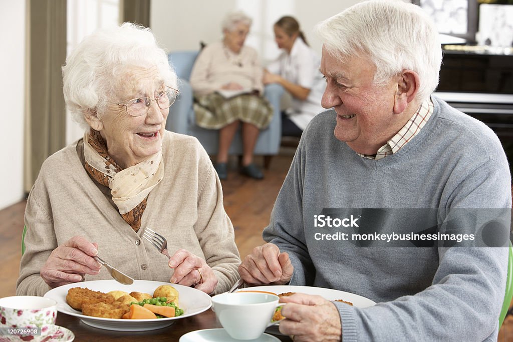 Smiling senior couple eating meal in care home Senior Couple Enjoying Meal Together In Care Home Senior Adult Stock Photo