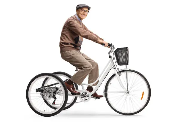 Cheerful elderly gentleman riding a tricycle and looking at camera isolated on white background