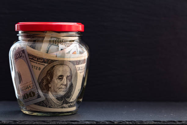 istock 100 dollar bills in jar on black background 1207271809