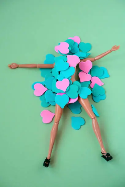 Photo of plastic doll lies under a pile of blue and pink hearts