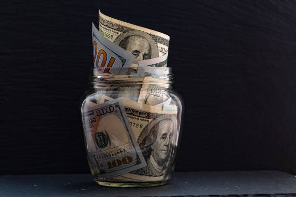 istock 100 dollar bills in jar on black background 1207272046