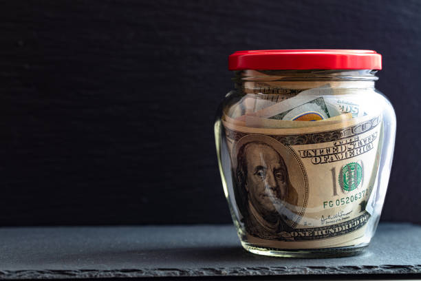 istock 100 dollar bills in jar on black background 1207272571