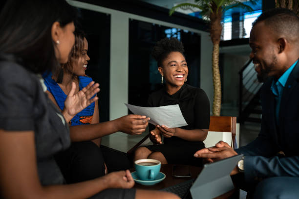 Laughing group of African businesspeople discussing paperwork in an office Laughing group of a young African businesspeople going over paperwork together during a casual meeting over coffee in an office north african ethnicity stock pictures, royalty-free photos & images
