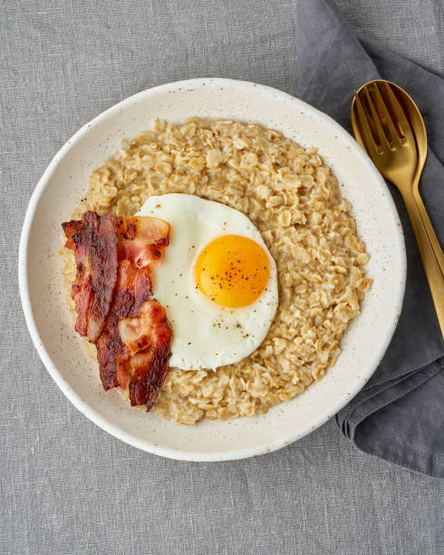 istock Oatmeal, fried egg and fried bacon. Hearty fat high-calorie breakfast, source of energy. Vertical 1207278003