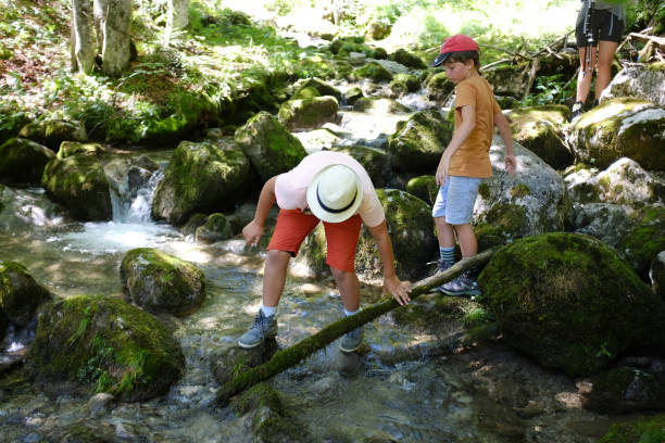 istock Two brothers in vibrant clothes standing on rocks in mountains spring in summer forest with water splashing and trying to make a crrosingg 1207280358