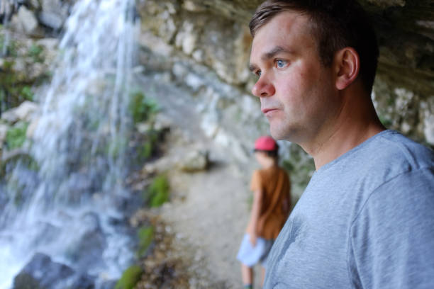 nahaufnahme eines hübschen kaukasischen mannes mit blauen augen, der neben einem wasserfall in den österreichischen alpen steht und ernst aussieht, müde ist. - travel destinations mountain hiking profile stock-fotos und bilder