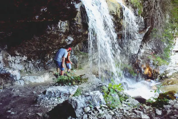 August 1, 2017 - Saalachtal, Austria: dad and boy under the waterfall on their hiking adventure in Alp mountains, Austria.