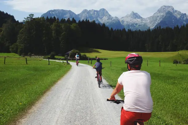August 3, 2017 - Mondsee, Austria: idyllic family togetherness time - dad riding bikes with his sons among the meadows and mountains range visible in the distance