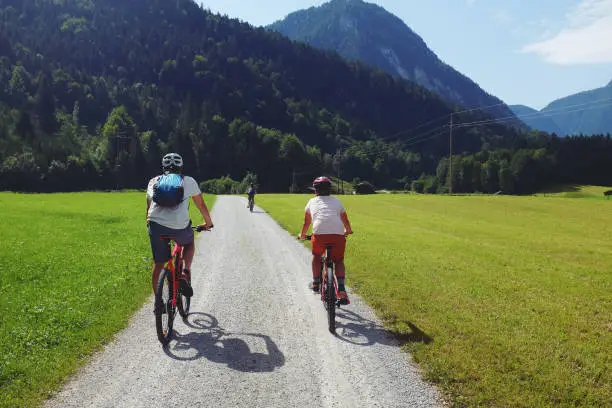 August 3, 2017 - Mondsee, Austria: caucasian father with a backpack and helmet riding side by side with his son on a narrow country road - being active and spending bonding time with his boys on vacation