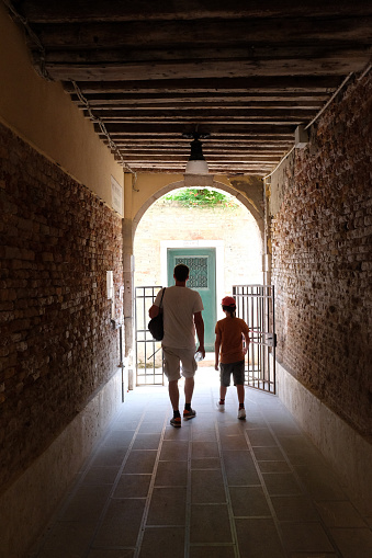 July 29, 2017 - Venice, Italy: man and a boy - dad and son - stepping from a dark tunnel into the light with their backs and silhouettes visible in Venice.
