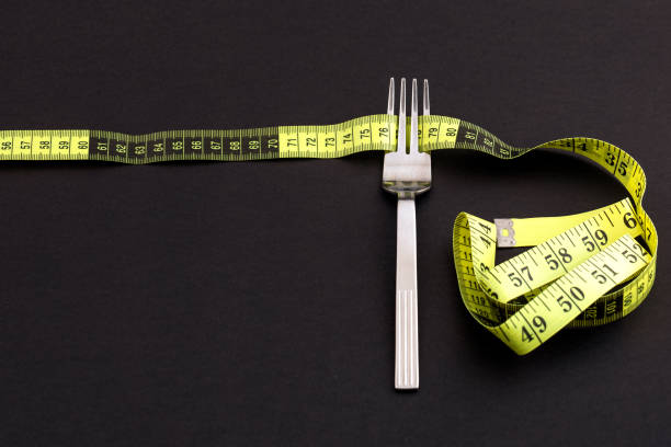 istock Fork with a measuring tape on a black background, diet or healthy eating concept 1207281998
