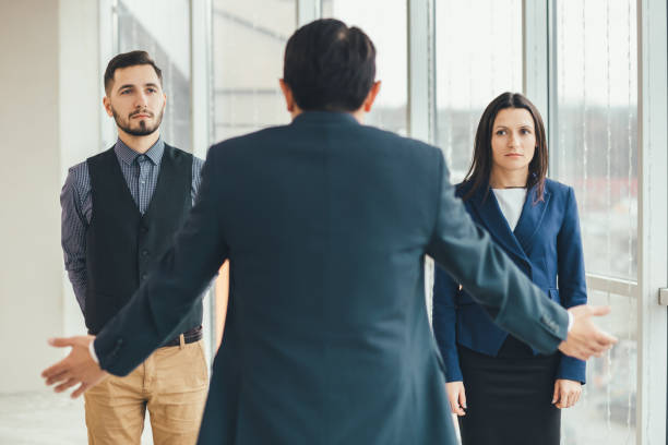istock Angry boss standing back to the camera, shouting at his workers, raising hand, while stressed employees standing, with guilty look on their faces. 1207288111