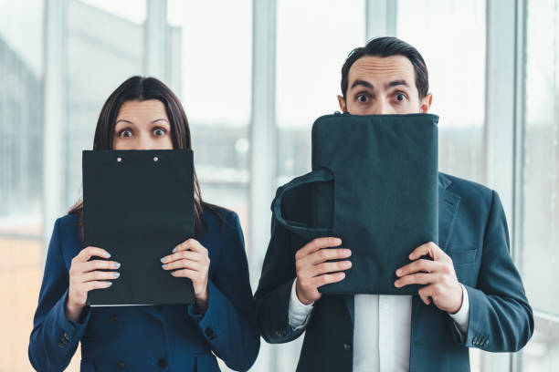 woman hiding her face behind clipboard, man hiding his face behind laptop case. - hiding humor occupation office imagens e fotografias de stock