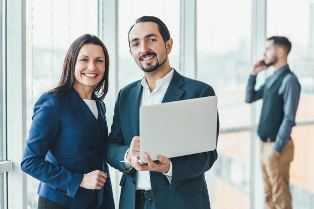 istock Successful man and woman making business plan, comparing annual data in laptop, while their coleague is on phone on blurred background. 1207289585