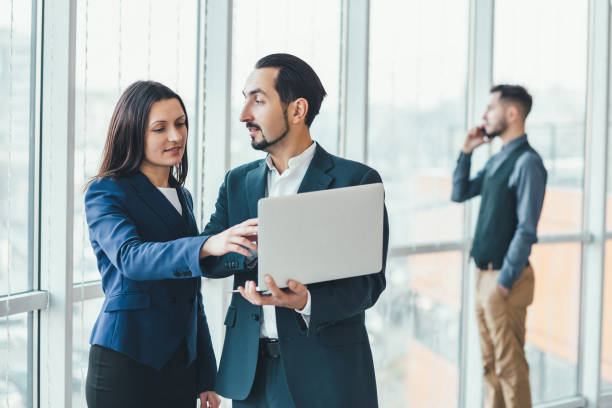 istock Successful man and woman making business plan, comparing annual data in laptop, while their coleague is on phone on blurred background. 1207290065