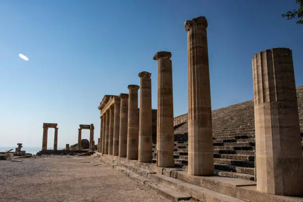 Photo of The Acropolis of Lindos in Rhodes, Greece at sunset. Scenic view of Doric columns from the ancient Temple of Athena Lindia setting sun light above the columns. Rhodes, Dodecanese, Greece, Europe