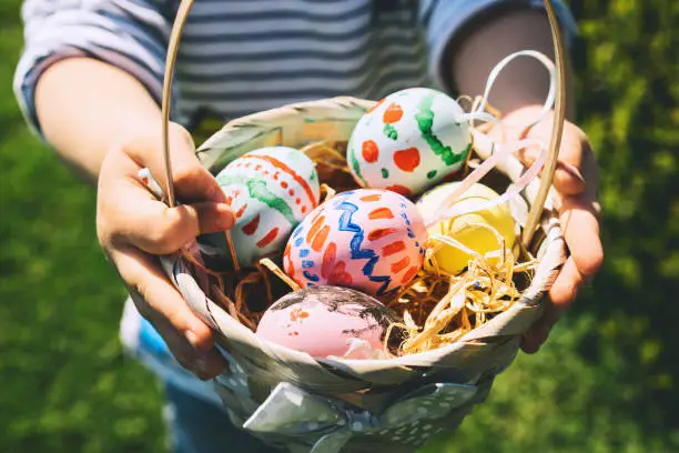 Colorful Easter eggs in basket. Children gathering painted decoration eggs in spring park. Kids hunt for egg outdoors. Festive family traditional play game on Easter.