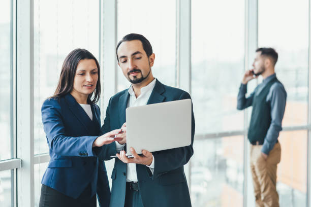 istock Successful man and woman making business plan, comparing annual data in laptop, while their coleague is on phone on blurred background. 1207291009