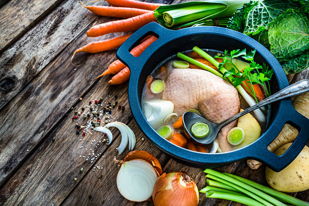 High angle view of a cooking pan filled with raw chicken bouillon ingredients shot on rustic kitchen table. Ingredients for preparing chicken broth like raw chicken, carrots, kale, potatoes, celery and onions are also all around the pan. The composition is at the right of an horizontal frame leaving useful copy space for text and/or logo at the left.\nHigh resolution 42Mp studio digital capture taken with SONY A7rII and Zeiss Batis 40mm F2.0 CF lens