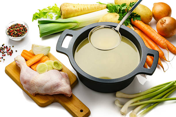 Chicken bouillon in a cooking pan with ingredients on white background