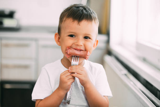 the child in the kitchen eating sausage and mashed potatoes on their own