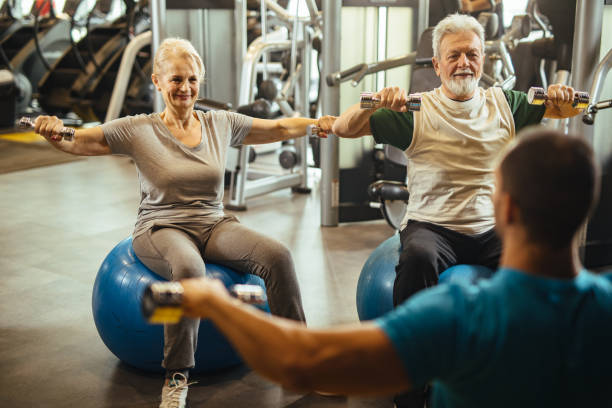 istock Senior couple exercising with personal trainer using dumbbells at the gym 1207295085