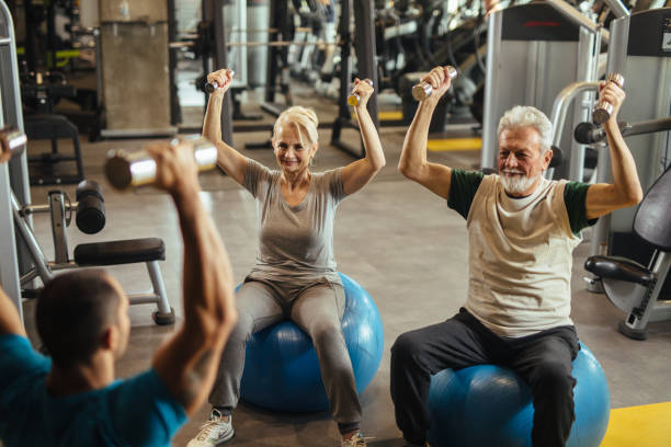 istock Senior couple exercising with personal trainer using dumbbells at the gym 1207296765
