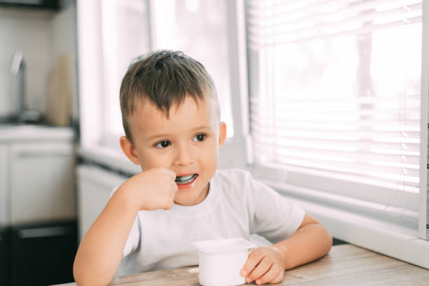 istock Cute boy in the kitchen eating yogurt from a white yogurt container, a place for advertising 1207296927