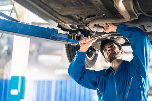 Photo of Vehicle service maintenance handsome mens checking under car condition on lifter hoist in garage. Automotive mechanic man use tool to tighten and replace damaged or broken part. Repair service concept