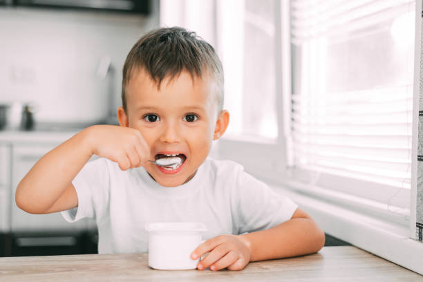 istock Cute boy in the kitchen eating yogurt from a white yogurt container, a place for advertising 1207297040