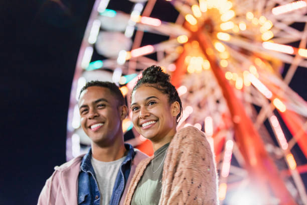 istock Young couple at county fair, by ferris wheel 1207300126