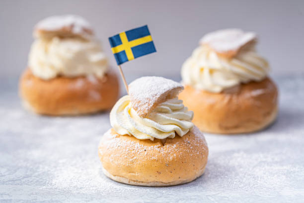 traditionelle skandinavische sahne und mandelpaste gefüllt kardamom brötchen semlor, mit einer schwedischen flagge. - shrove tuesday stock-fotos und bilder