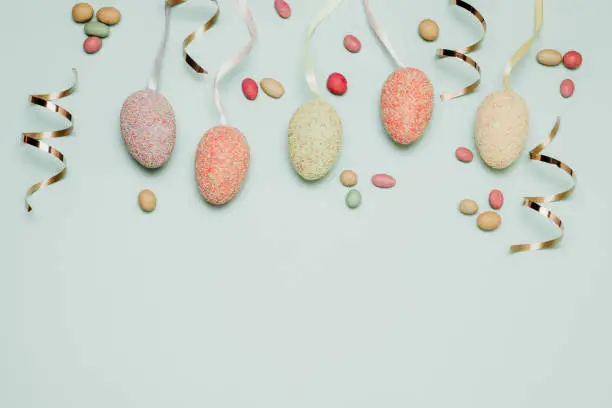 Holiday concept with multicolored easter eggs, dragee candies and gold candy on a blue background, top view