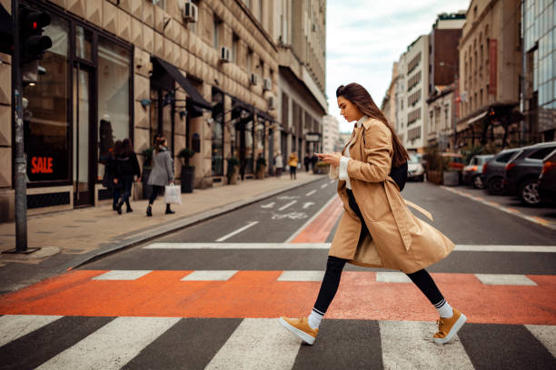 Pretty woman crossing the street Beautiful young woman looking bothered, texting on her phone while crossing the street street fashion stock pictures, royalty-free photos & images