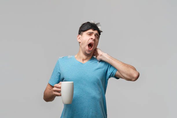 istock Young brunet man with sleep mask holding white cup with coffee isolated over grey background. 1207304634