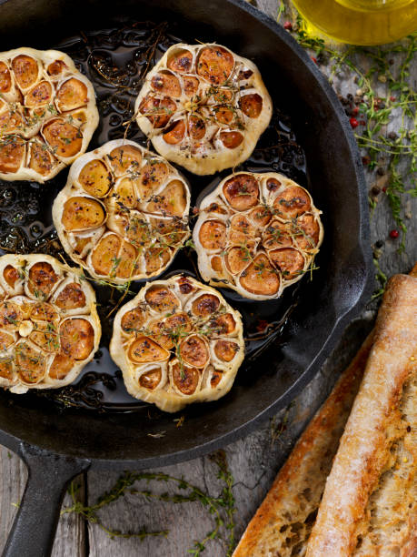 обжаренный чеснок с солью, перцем, тимьяном и оливковым маслом в чугунной сковороде - roast garlic стоковые фото и изображения