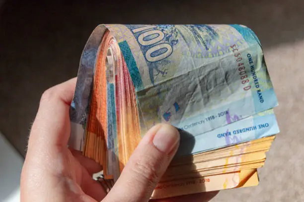 Photo of A close up view of one and two hundred rand notes folded over in a young womens hand