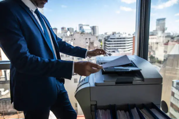 Side view of Latin businessman copying paper document on photocopier machine in office