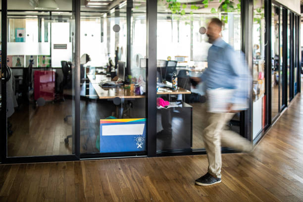 Mature well-dressed businessman walking in modern office space with paper documents under hand, blurred motion