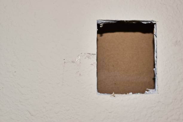 Damaged white drywall prepped for hole repairs. Section of damaged white drywall with square cut out of it for replacement. Copy space on the left side of image. Repair, DIY home maintenance. painted drywall texture stock pictures, royalty-free photos & images
