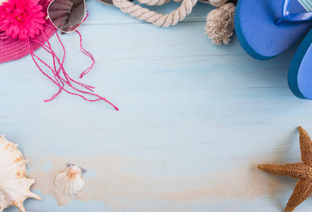 istock Beach holidays concept. Seashells, starfish, sunglasses, hat and flip flop on light blue background with sand. 1207310379