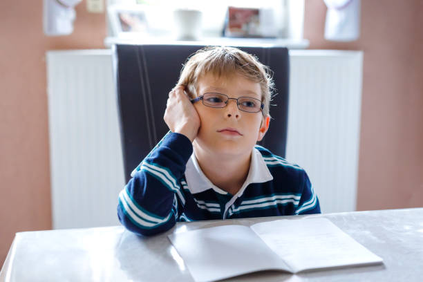 自宅で宿題を作るメガネを持つ思慮深い小さな子供の男の子は、カラフルなペンでテキストを書きます。小さな子供が運動をしている、屋内で。小学校・教育 - elementary student little boys classroom child ストックフォトと画像