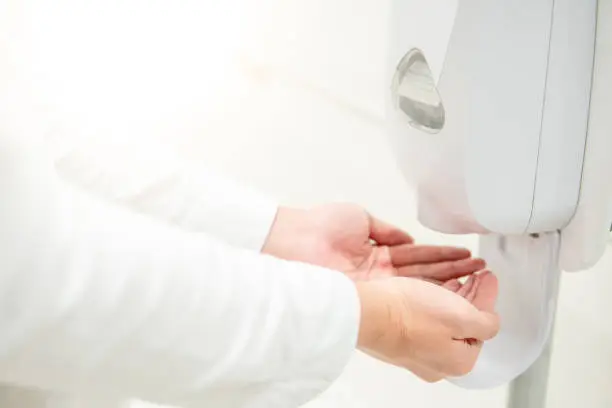 Male patient hands using automatic alcohol dispenser for cleaning hand in the hospital. Infection prevention concept. Save and clean in public medical center area.